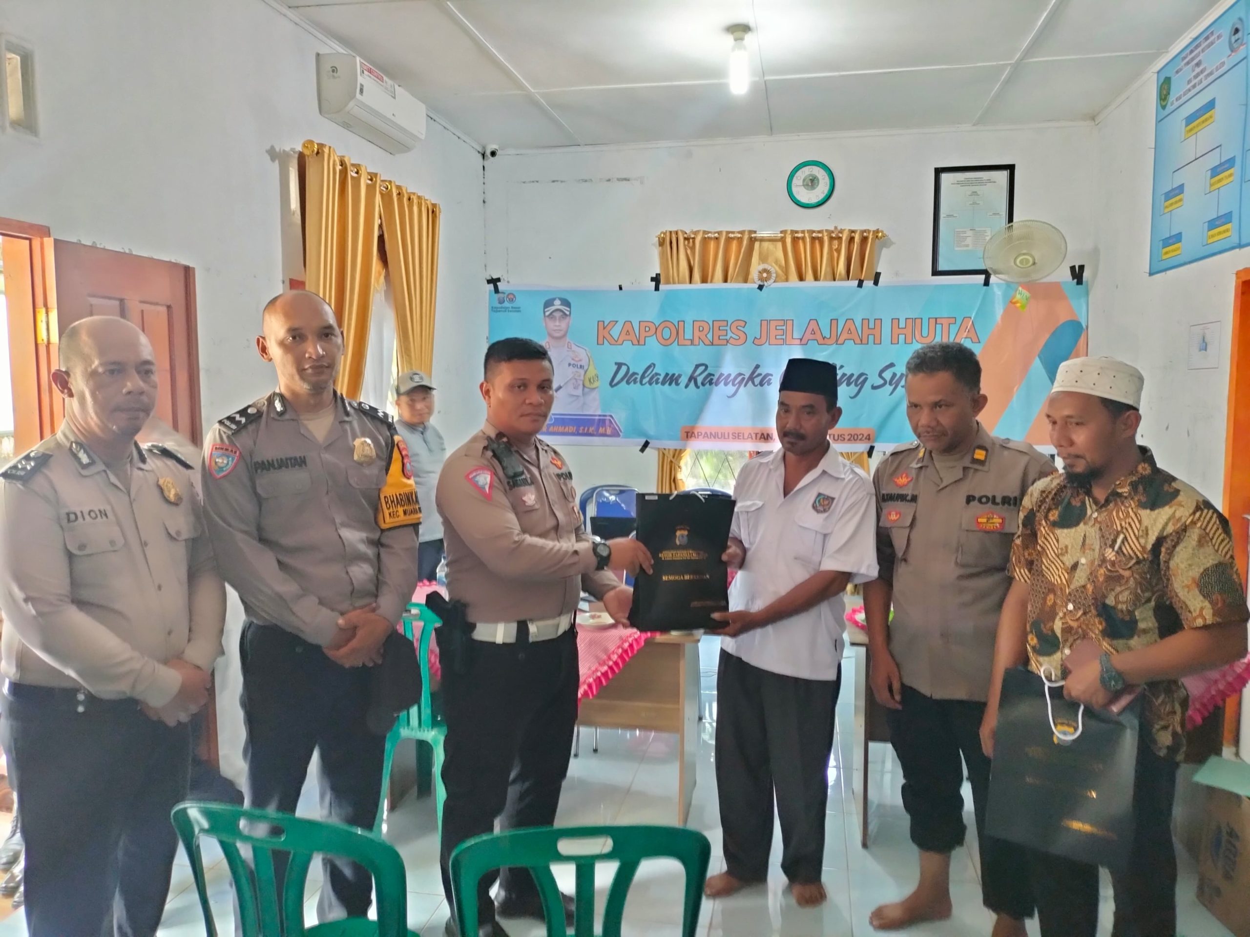 Kanit Gakkum Sat Lantas Polres Tapsel, Ipda Samuel Jefri Hutapea, bersama Waka Polsek Batang Toru, Iptu Taufik Simanullang, saat menyerahkan souvenir ke perwakilan perangkat Desa yang hadir dalam gerakan Kapolres Jelajah Huta
