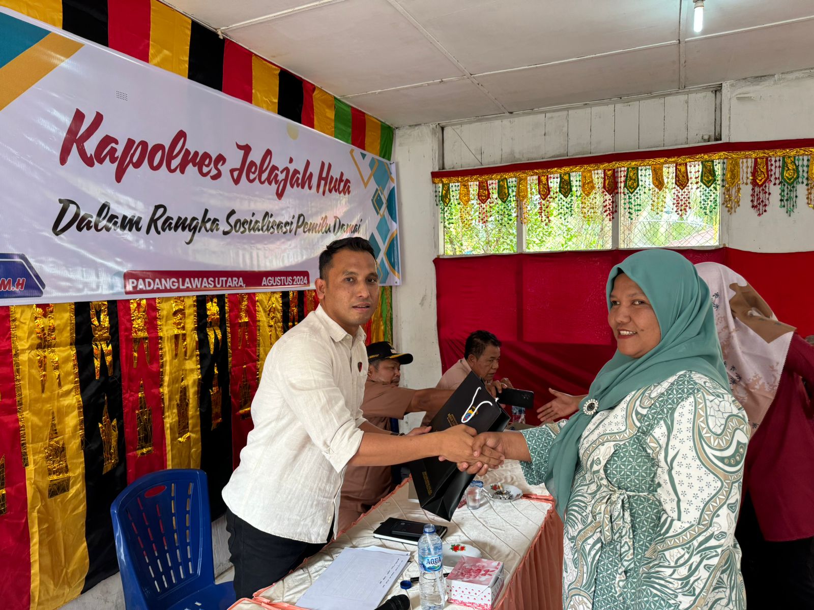 Kanit Tipiter Sat Reskrim Polres Tapsel, Ipda Ilham P Nasution, saat menyerahkan souvenir ke perwakilan masyarakat di sela gerakan Kapolres Tapsel Jelajah Huta di Kabupaten Paluta