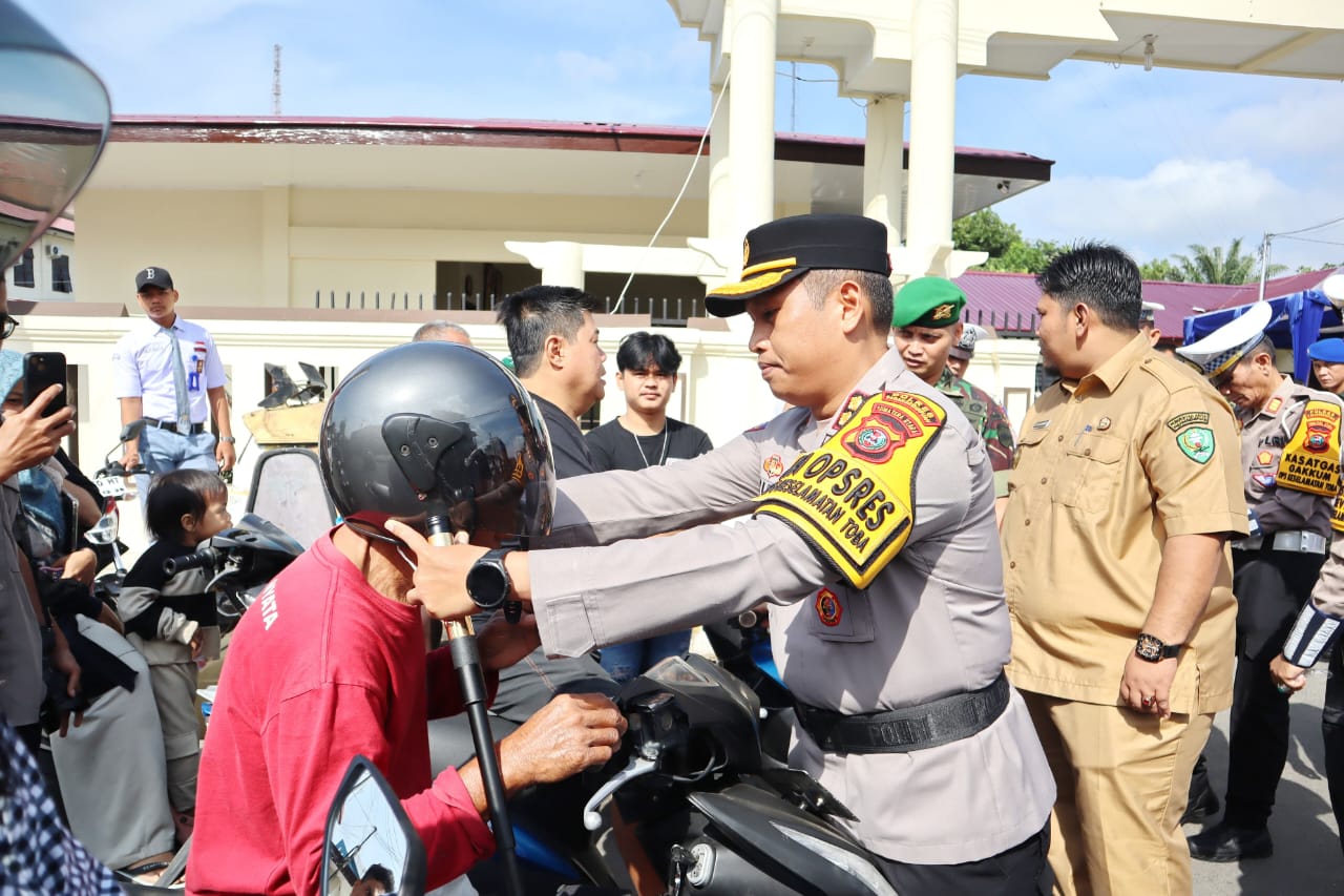 Kapolres Padangsidimpuan, AKBP Wira Prayatna, menyerahkan helm gratis ke pengendara roda dua yang melintas tanpa memakai helm usai Apel gelar pasukan Ops Keselamatan Toba 2025