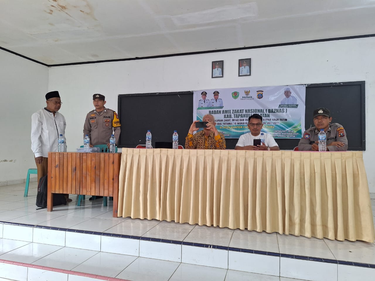 Personel Polsek Batang Toru, Aiptu Andi Siregar, saat melakukan pengamanan kegiatan penyaluran zakat, infaq, dan DSKL digelar di Aula Kantor Camat setempat