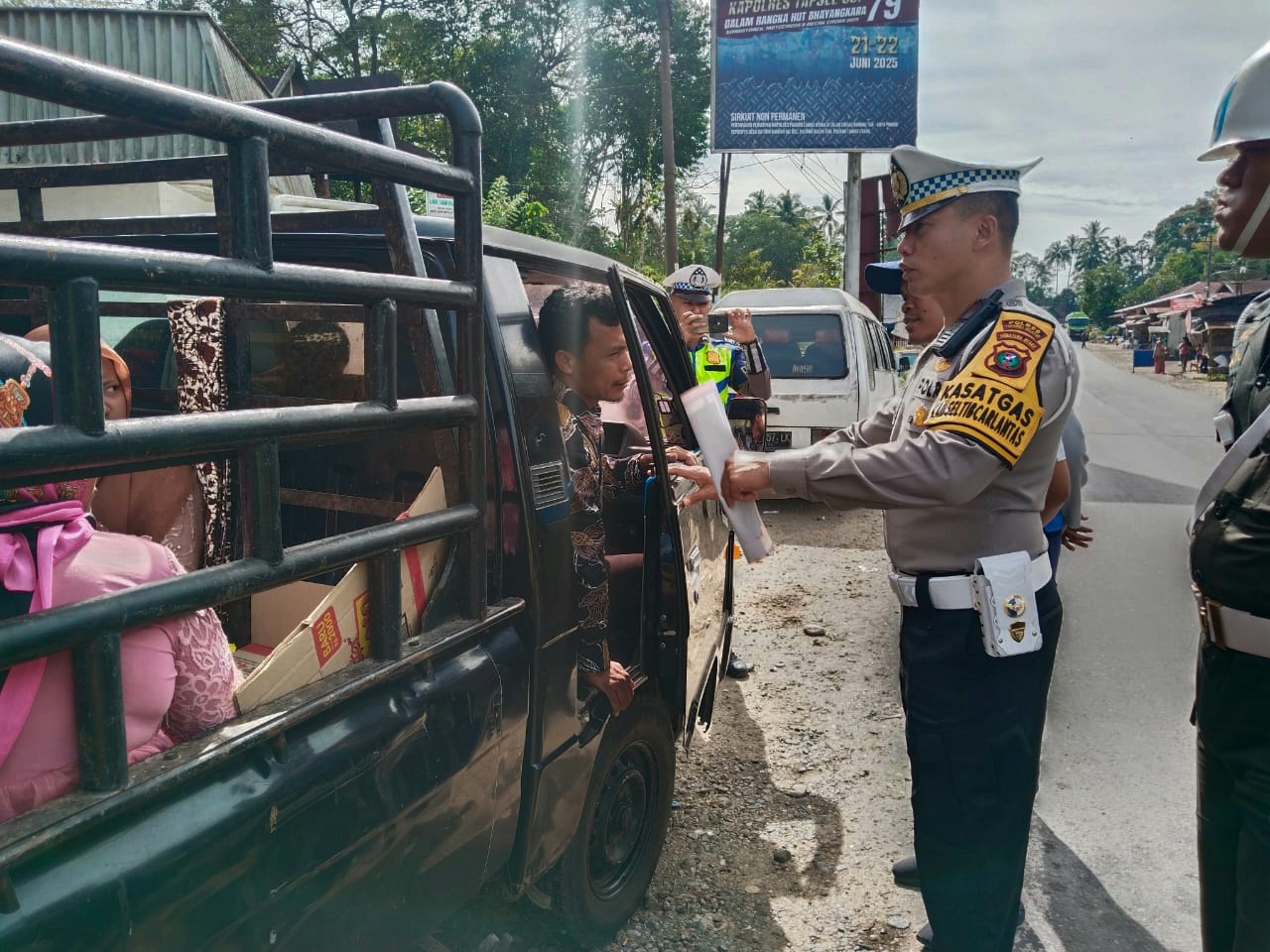 Kasat Lantas Polres Tapsel, AKP Dahnial Saragih, saat membagikan brosur dan menempelkan stiker terkait keselamatan berlalu lintas ke salah satu pengguna jalan yang melintas di sela Operasi Patuh Toba 2025
