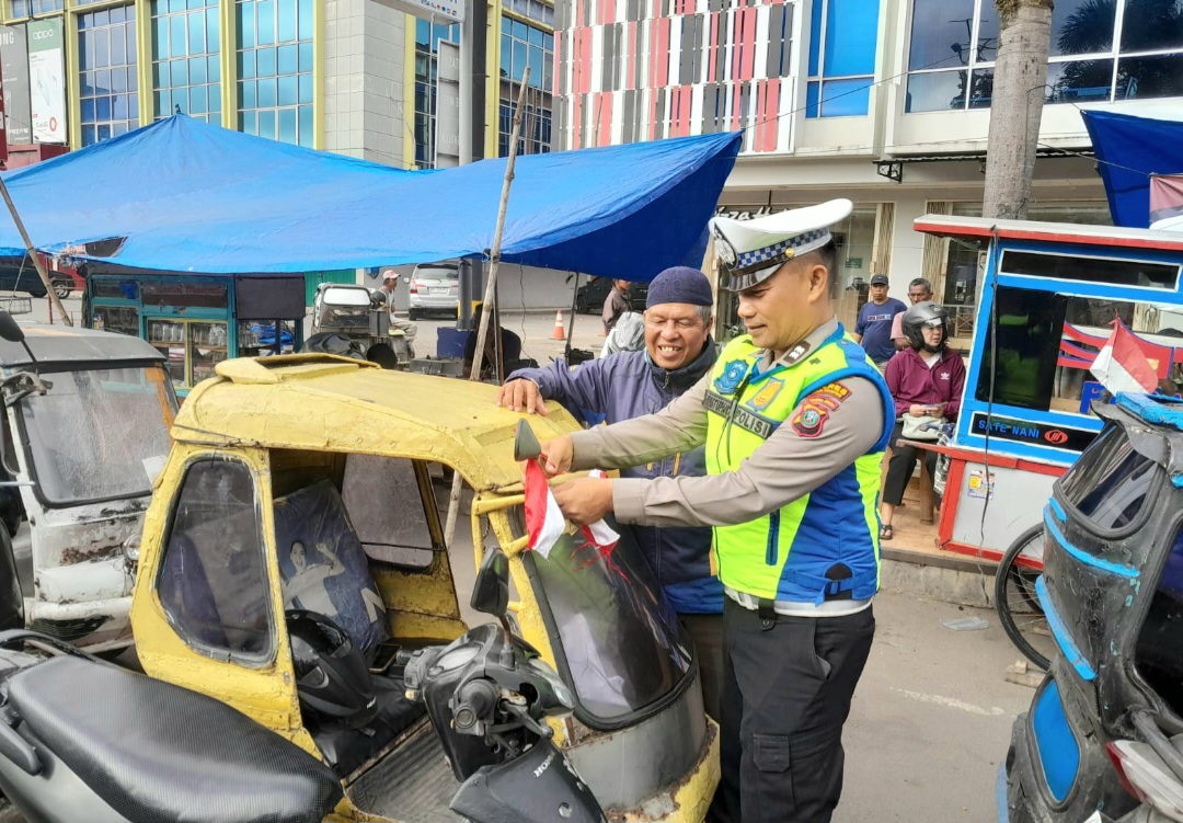 Personel Polantas Polres Padangsidimpuan terlihat tersenyum hangat saat menyerahkan bendera merah putih ke pengendara becak bermotor di Jalan Sudirman