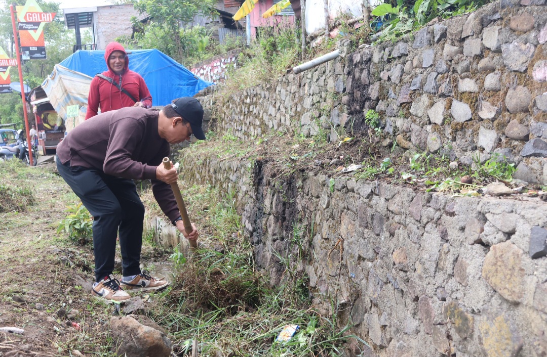 Bupati Tapsel, Gus Irawan Pasaribu, memegang cangkul untuk membersihkan rumput di Desa Paran Dolok Mardomu saat momen WCD 2025